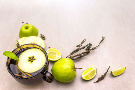 Fruit tea concept. Fresh lime and apple, dry herbs. Glass brown cup on stone background.の写真素材