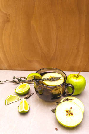 Fruit tea concept. Fresh lime and apple, dry herbs. Glass brown cup on wooden and stone background.の写真素材