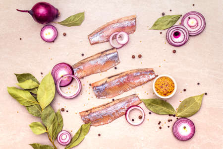 Fillet of pickled Norwegian salted herring with spices and onions. Marinated fish on a stone background, top view.の写真素材