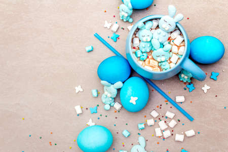Easter kids hot sweet chocolate or cocoa with funny marshmallow bunny rabbits and easter eggs. On sand stone background, cope space, top view, close up.の写真素材