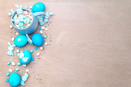 Easter kids hot sweet chocolate or cocoa with funny marshmallow bunny rabbits and easter eggs. On sand stone background, top view, cope space.の写真素材