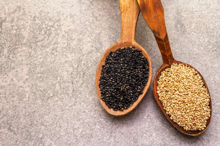 White and black sesame seeds in wooden spoons on stone background, top view, close upの写真素材