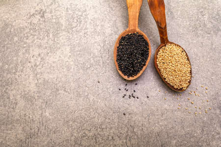 White and black sesame seeds in wooden spoons on stone background, top view, close upの写真素材