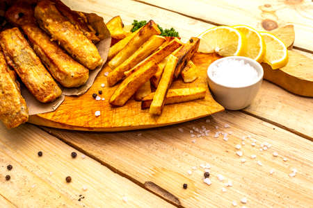 Fish and chips on wooden board in parchment paper on table. Traditional British food, close up