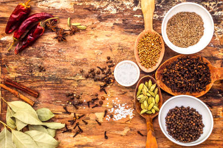 Set of different spices and herbs - black pepper, allspice, cumin, hot pepper, bay leaf, coriander, cardamom, star anise, cinnamon sticks, salt. On wooden bark background, top view.の写真素材