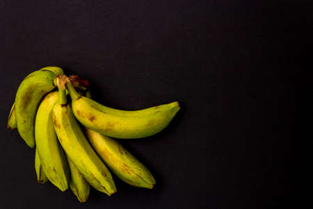 A bunch of ripe yellow-green bananas isolated on a black background, top view.