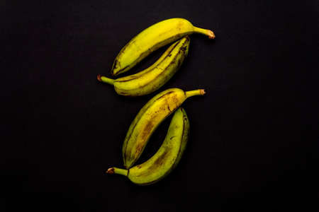 Several ripe yellow-green bananas isolated on a black background, top view.の写真素材