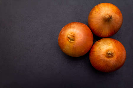Three large yellow onion on black background, top view.
