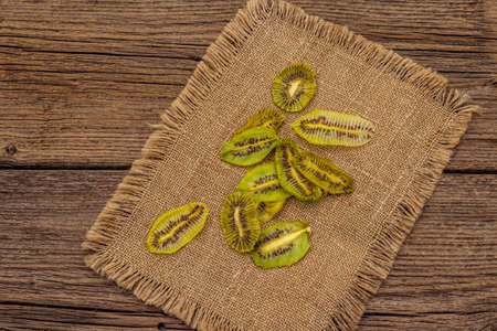 Dried slices of kiwi. Fruit snack, healthy eating concept. Sackcloth, old wooden boards background, top view, copy spaceの写真素材