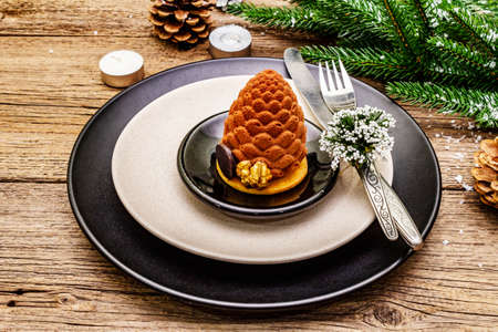 Christmas and New Year dinner place setting. Sweet snack, fir tree branch, candles, cones, ceramic plates, fork and knife. Winter cutlery wooden background, close upの写真素材