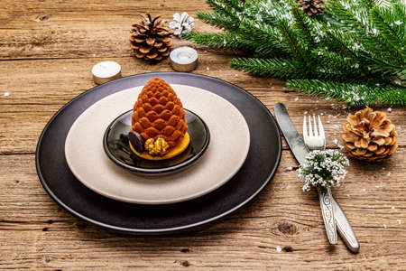 Christmas and New Year dinner place setting. Sweet snack, fir tree branch, candles, cones, ceramic plates, fork and knife. Winter cutlery wooden background, close upの写真素材