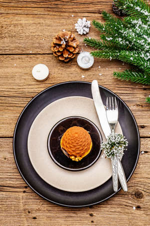 Christmas and New Year dinner place setting. Sweet snack, fir tree branch, candles, cones, ceramic plates, fork and knife. Winter cutlery wooden background, copy space, top viewの写真素材