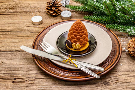 Christmas and New Year dinner place setting. Sweet snack, fir tree branch, candles, cones, ceramic plates, fork and knife. Winter cutlery wooden background, close upの写真素材