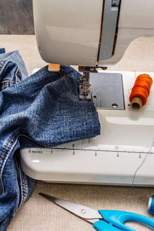 Sewing machine foot on denim. Scissors, spools of thread. Stands on a table, wooden backdropの写真素材