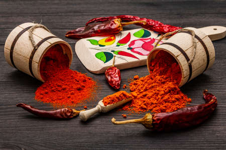 Magyar (Hungarian) red sweet and hot paprika powder. Traditional pattern on a cutting board, different varieties of dry pepper. Black wooden background, close upの写真素材