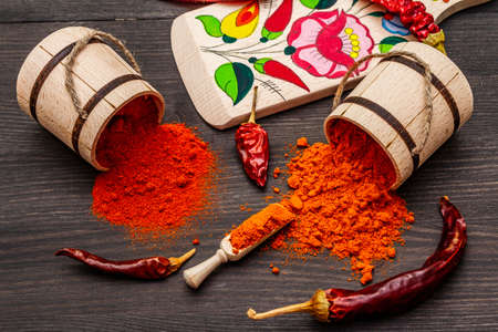 Magyar (Hungarian) red sweet and hot paprika powder. Traditional pattern on a cutting board, different varieties of dry pepper. Black wooden background, close upの写真素材
