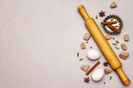 Christmas cooking background, spices, eggs, brown lump sugar, cupcake baking dish and a rolling pin. Light stone concrete background, top view, copy spaceの写真素材