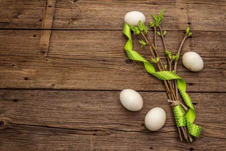 Zero waste Easter concept. Spring twigs with fresh green leaves, wooden eggs, polka dot ribbon. Old vintage wooden boards background, copy space, top view, flat layの写真素材