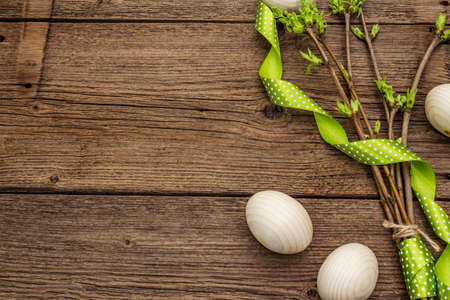 Zero waste Easter concept. Spring twigs with fresh green leaves, wooden eggs, polka dot ribbon. Old vintage wooden boards background, close up, copy space, top viewの写真素材