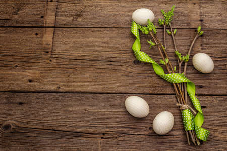 Zero waste Easter concept. Spring twigs with fresh green leaves, wooden eggs, polka dot ribbon. Old vintage wooden boards background, copy space, top view, flat layの写真素材