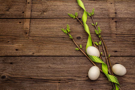 Zero waste Easter concept. Spring twigs with fresh green leaves, wooden eggs, polka dot ribbon. Old vintage wooden boards background, copy space, top view, flat layの写真素材