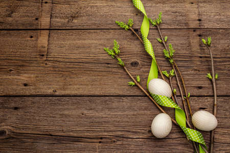 Zero waste Easter concept. Spring twigs with fresh green leaves, wooden eggs, polka dot ribbon. Old vintage wooden boards background, copy space, top view, flat layの写真素材