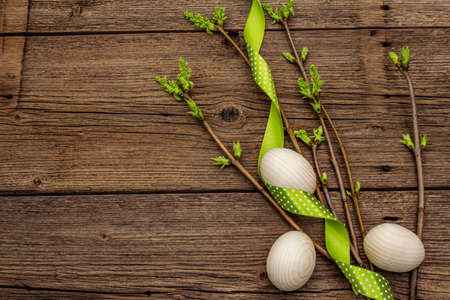 Zero waste Easter concept. Spring twigs with fresh green leaves, wooden eggs, polka dot ribbon. Old vintage wooden boards background, close up, copy space, top viewの写真素材