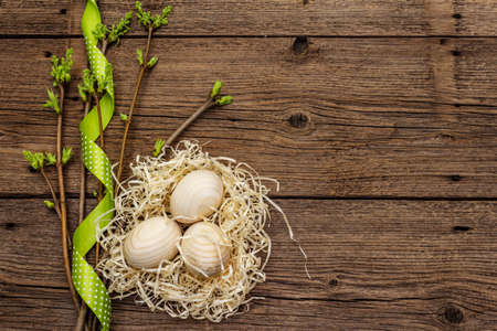 Zero waste Easter concept. Spring twigs with fresh green leaves, wooden eggs in nest, polka dot ribbon. Old vintage wooden boards background, copy space, top viewの写真素材