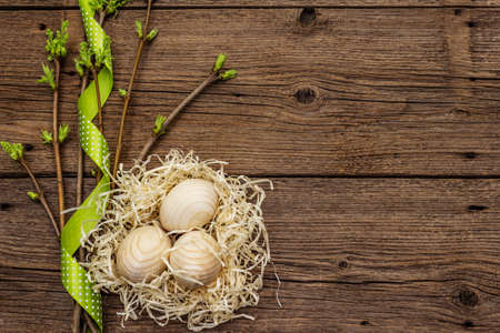Zero waste Easter concept. Spring twigs with fresh green leaves, wooden eggs in nest, polka dot ribbon. Old vintage wooden boards background, copy space, top viewの写真素材