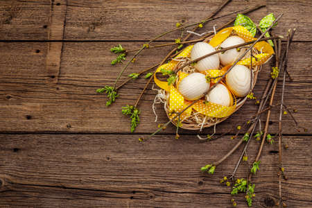 Zero waste Easter concept. Spring twigs with fresh green leaves, wooden eggs in basket, polka dot ribbon. Old vintage wooden boards background, copy space, top viewの写真素材