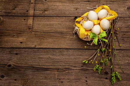Zero waste Easter concept. Spring twigs with fresh green leaves, wooden eggs in basket, polka dot ribbon. Old vintage wooden boards background, copy space, top viewの写真素材