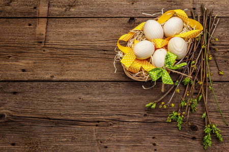 Zero waste Easter concept. Spring twigs with fresh green leaves, wooden eggs in basket, polka dot ribbon. Old vintage wooden boards background, copy space, top viewの写真素材