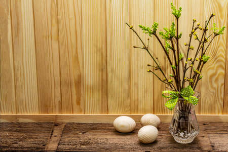 Zero waste Easter concept. Spring twigs with fresh green leaves. Glass vase, wooden eggs, polka dot ribbon. Wooden boards background and backdrop, copy spaceの写真素材