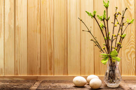 Zero waste Easter concept. Spring twigs with fresh green leaves. Glass vase, wooden eggs, polka dot ribbon. Wooden boards background and backdrop, copy spaceの写真素材