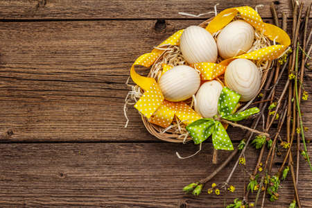 Zero waste Easter concept. Spring twigs with fresh green leaves, wooden eggs in basket, polka dot ribbon. Old vintage wooden boards background, copy space, top view, close upの写真素材