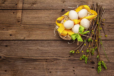 Zero waste Easter concept. Spring twigs with fresh green leaves, wooden eggs in basket, polka dot ribbon. Old vintage wooden boards background, copy space, top viewの写真素材