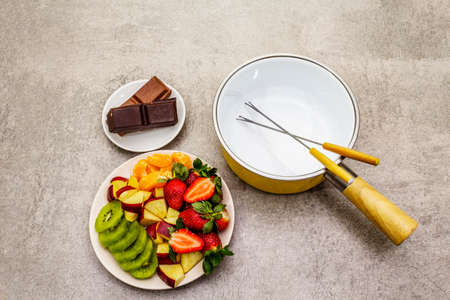 Chocolate fondue. Assorted fresh fruits, two types of chocolate. Ingredients for cooking a sweet romantic dessert. Stone concrete backgroundの写真素材