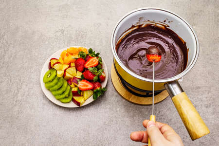 Chocolate fondue. Assorted fresh fruits, two types of chocolate, male hand. Ingredients for cooking a sweet romantic dessert. Stone concrete backgroundの写真素材