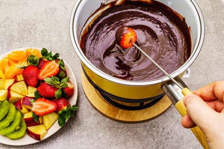 Chocolate fondue. Assorted fresh fruits, two types of chocolate, male hand. Ingredients for cooking a sweet romantic dessert. Stone concrete backgroundの写真素材