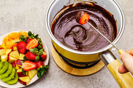 Chocolate fondue. Assorted fresh fruits, two types of chocolate, male hand. Ingredients for cooking a sweet romantic dessert. Stone concrete backgroundの写真素材