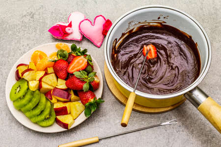 Chocolate fondue. Assorted fresh fruits, two types of chocolate, felt hearts. Ingredients for cooking a sweet romantic dessert. Stone concrete backgroundの写真素材