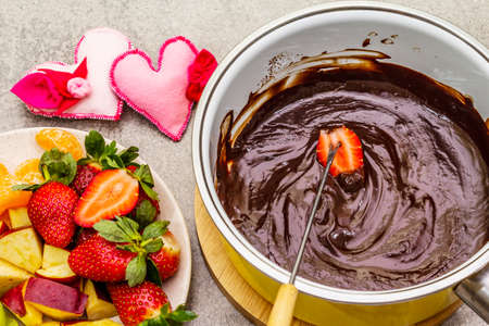 Chocolate fondue. Assorted fresh fruits, two types of chocolate, felt hearts. Ingredients for cooking a sweet romantic dessert. Stone concrete backgroundの写真素材