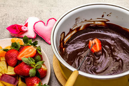 Chocolate fondue. Assorted fresh fruits, two types of chocolate, felt hearts. Ingredients for cooking a sweet romantic dessert. Stone concrete backgroundの写真素材