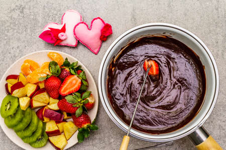 Chocolate fondue. Assorted fresh fruits, two types of chocolate, felt hearts. Ingredients for cooking a sweet romantic dessert. Stone concrete backgroundの写真素材