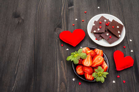 Valentine's Day romantic concept. Chocolate, fresh ripe strawberry, red felt hearts. Sweet dessert for lovers. Black wooden background, top view, copy spaceの写真素材