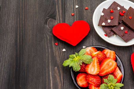 Valentine's Day romantic concept. Chocolate, fresh ripe strawberry, red felt hearts. Sweet dessert for lovers. Black wooden background, top view, copy spaceの写真素材