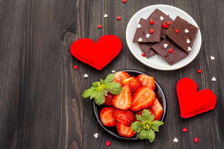 Valentine's Day romantic concept. Chocolate, fresh ripe strawberry, red felt hearts. Sweet dessert for lovers. Black wooden background, top view, copy spaceの写真素材