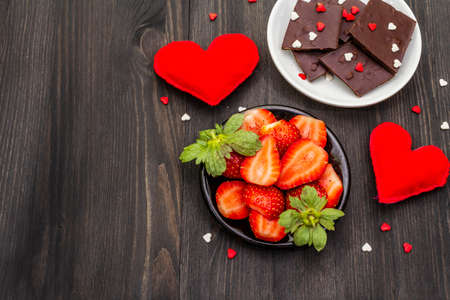 Valentine's Day romantic concept. Chocolate, fresh ripe strawberry, red felt hearts. Sweet dessert for lovers. Black wooden background, top view, copy spaceの写真素材