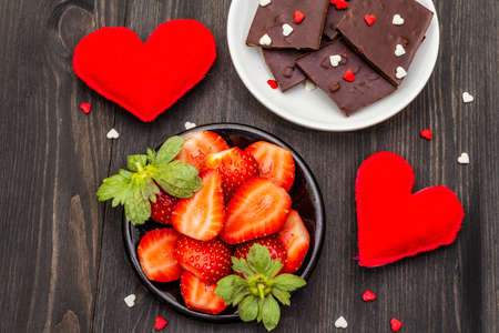 Valentine's Day romantic concept. Chocolate, fresh ripe strawberry, red felt hearts. Sweet dessert for lovers. Black wooden background, top view, close upの写真素材