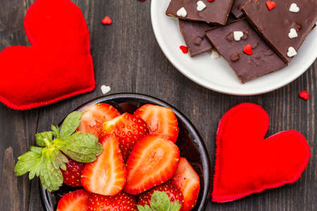 Valentine's Day romantic concept. Chocolate, fresh ripe strawberry, red felt hearts. Sweet dessert for lovers. Black wooden background, top view, close upの写真素材